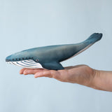 A Bumbu Blue whale wooden toy figure placed on the palm of an adult's hand to show scale. 