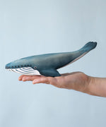 A Bumbu Blue whale wooden toy figure placed on the palm of an adult's hand to show scale. 