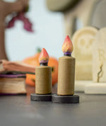 Bumbu Toys wooden Candle figures Set. The candles have a beige colour, on a black coloured base with a flame on the top. One candle is taller than the other. The candles are placed at the front and centre of a Halloween themed small world play set up. 