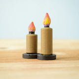 Bumbu Toys wooden Candle figures Set. The candles have a beige colour, on a black coloured base with a flame on the top. One candle is taller than the other. The candles are placed on a wooden surface. 