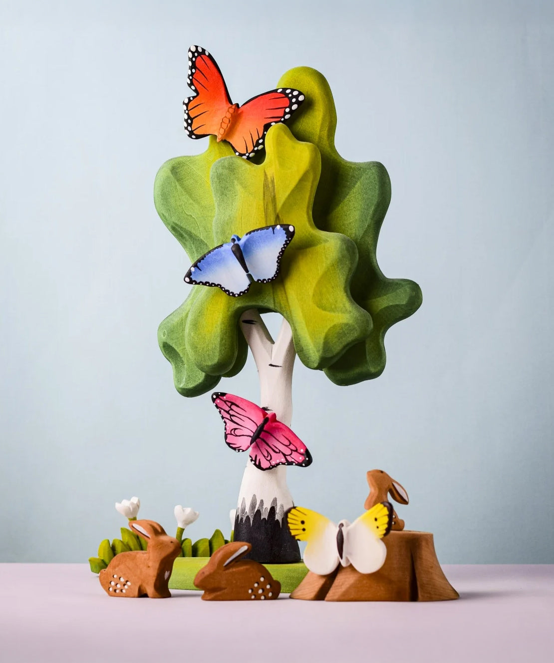 Bumbu Toys wooden Butterflies, placed on a Bumbu Birch Tree surrounded by Bumbu Rabbits, flowers and grass.