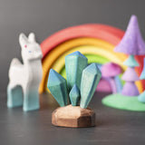 A Bumbu toys crystals placed at the front of a small world play scene. Other wooden toys and figure can be seen blurred in the background. 