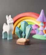A Bumbu toys crystals placed at the front of a small world play scene. Other wooden toys and figure can be seen blurred in the background. 
