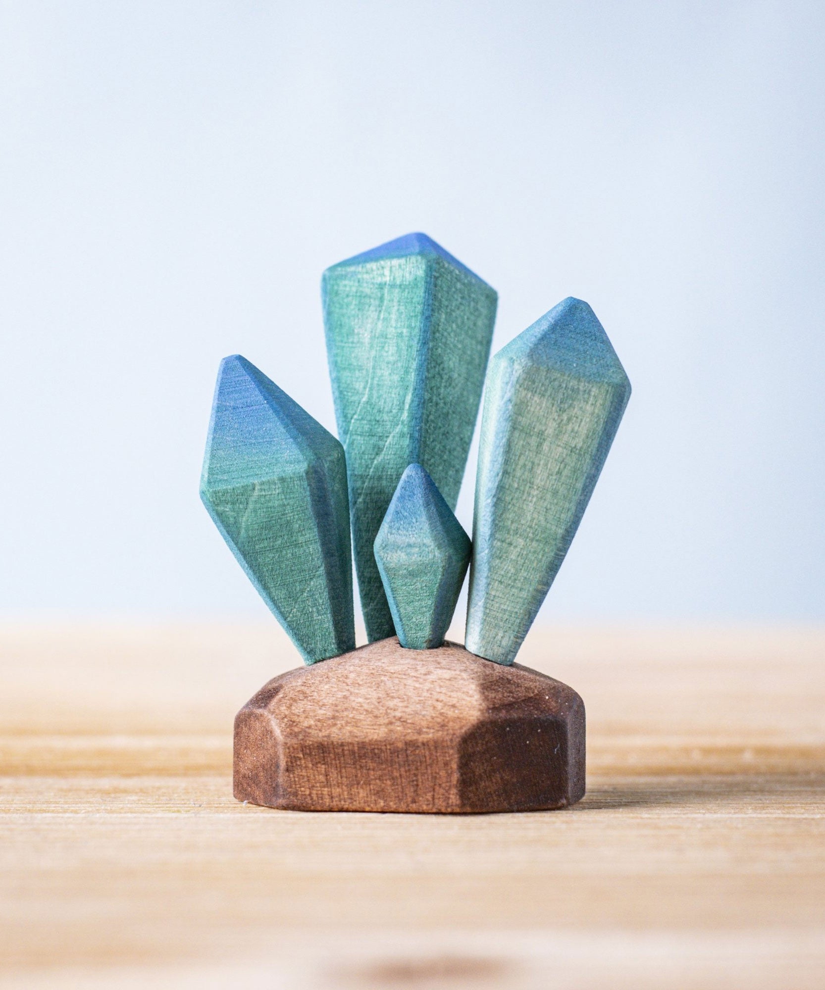 A Bumbu Toys Crystals wooden figure placed on a wooden surface. These handmade wooden crystals are perfect for use in setting scenes and small world play or just for decoration and display. Check out our full range of wooden toy scenery at Babipur. 