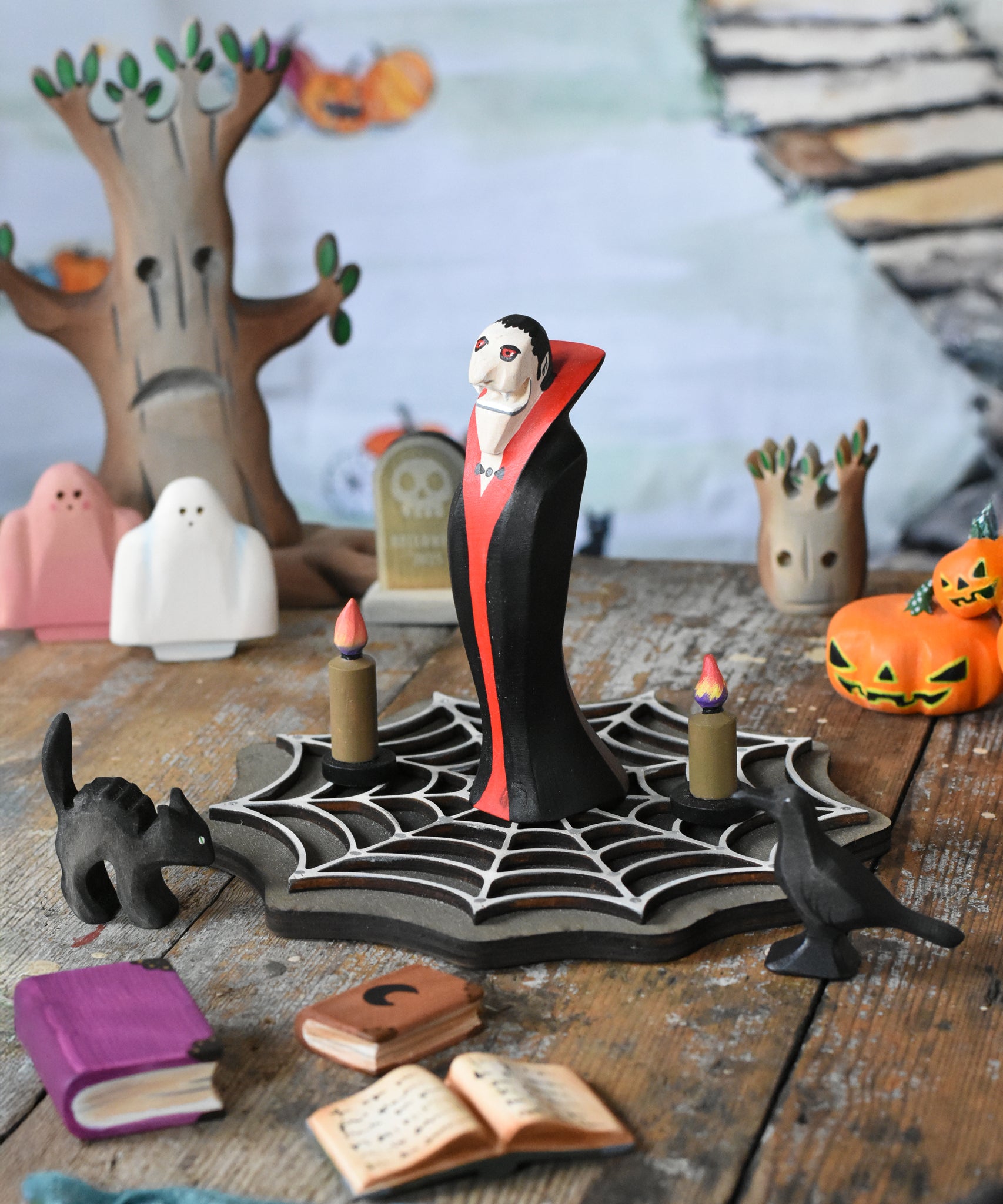 Bumbu Toys Dracula The Vampire Wooden Halloween Figure placed on a wooden cobweb in the middle of a small world play scene with Bumbu Halloween and Autumn themed toys.
These expertly hand crafted items are part of a large range of wooden toys available here at Babipur.  
