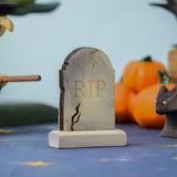 The RIP decorated headstone from the Bumbu Toys Gravestones Set, the gravestone has crack detailing on the edges giving it a spooky Halloween vibe. The headstone is pictured in a Halloween themed play scene. 