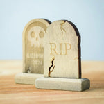 Bumbu Toys Gravestones Set. The set contains two headstones, one is decorated with RIP in large letters the other had a skull with Halloween 2024 written underneath. The Headstones are placed on a wooden surface.