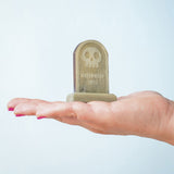 The skull decorated headstone from the Bumbu Toys Gravestones Set. The headstone is placed on an adult's hand.