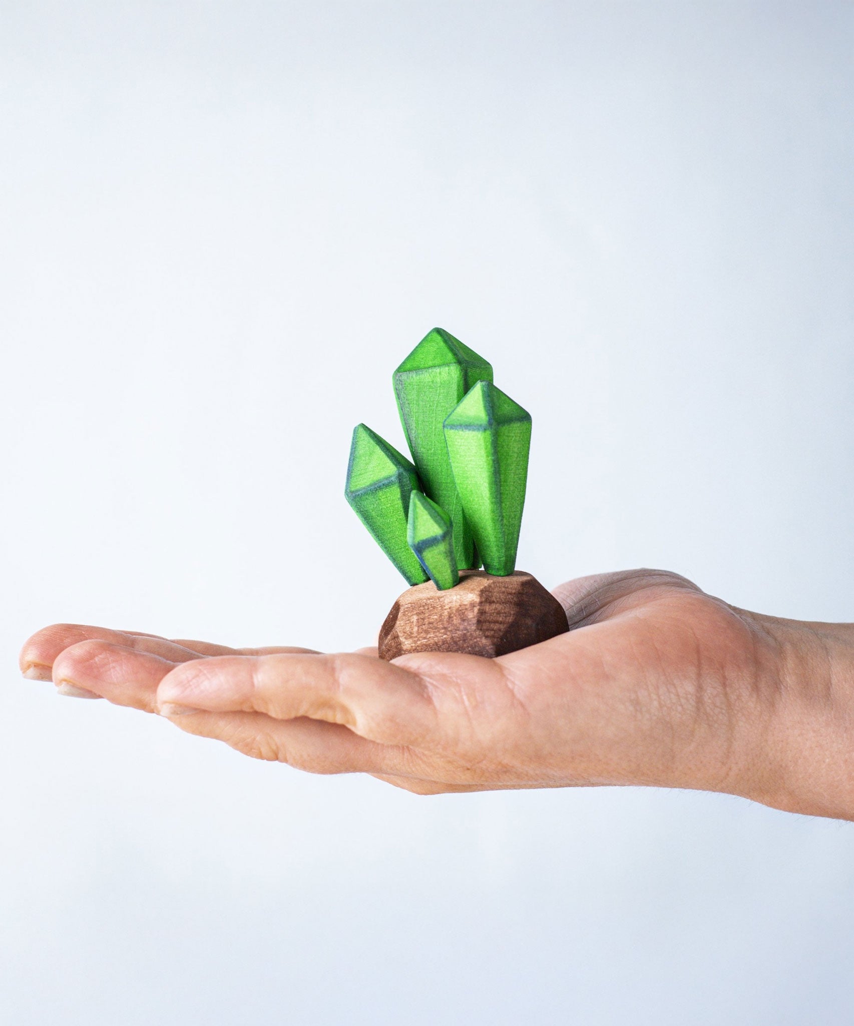 The green coloured Bumbu wooden toy crystals placed on the palm of an adult's hand to show scale. These handmade toys are perfect for adding to scenery on small world play scenes and just as beautiful on display too.