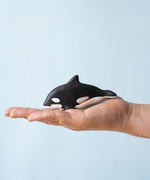 A Bumbu Toys Baby Orca placed on the palm of an adult's hand to show scale.