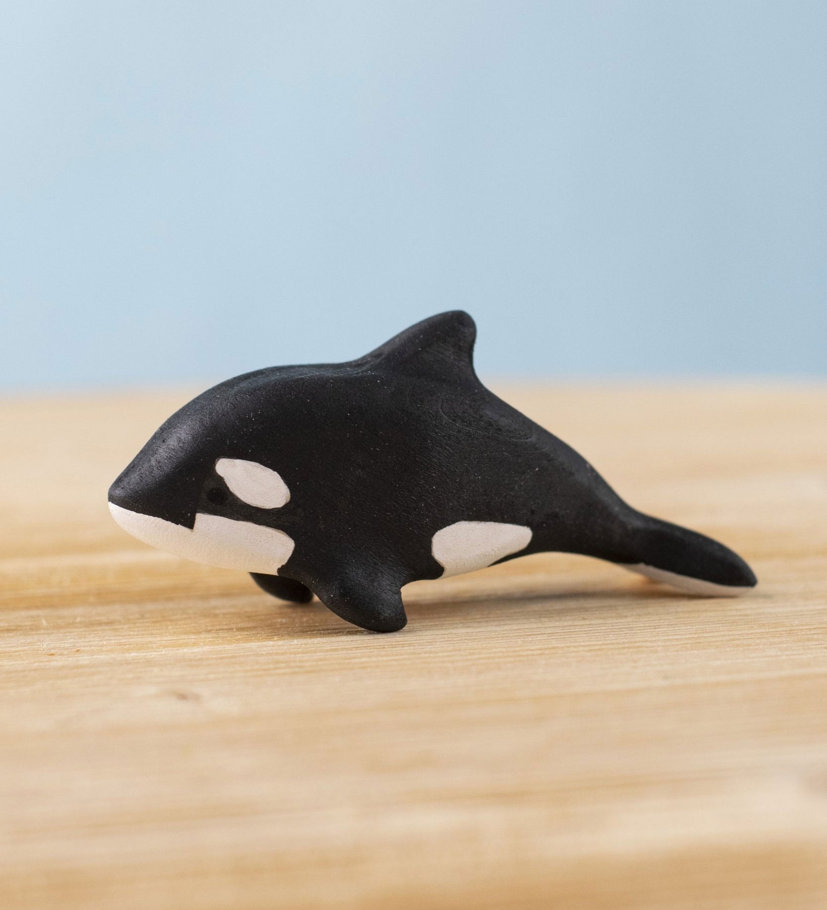 A Bumbu Toys Baby Orca placed on a wooden toy surface. 