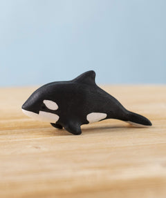 A Bumbu Toys Baby Orca placed on a wooden toy surface. 