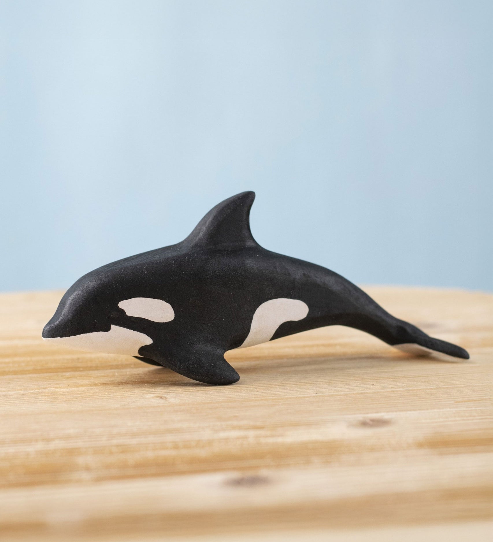 A Bumbu Toys Orca handmade wooden toy figure placed on a wooden surface. The Orca whale is part of a large range of handmade wooden toys here at Babipur.