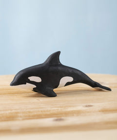 A Bumbu Toys Orca handmade wooden toy figure placed on a wooden surface. The Orca whale is part of a large range of handmade wooden toys here at Babipur.