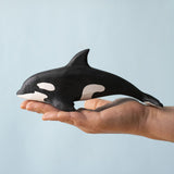 A Bumbu Toys Orca handmade wooden toy figure placed on the palm of an adult's hand. The Orca whale is part of a large range of handmade wooden toys here at Babipur.