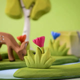 Bumbu small wooden grass with pink flower placed at the front of a small world play scene with deer, flowers and trees in the background.
