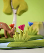 Bumbu small wooden grass with pink flower placed at the front of a small world play scene with deer, flowers and trees in the background.