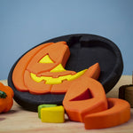 The Bumbu Halloween Pumpkin Round Wooden Puzzle pictured on it's black coloured base frame. The puzzle is propped up on it's side on a wooden surface.
