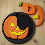 The Bumbu Halloween Pumpkin Round Wooden Puzzle pictured on it's black coloured base frame with 4 of the pieces taken out. The puzzle is pictured from above on a wooden surface.