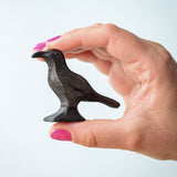 Bumbu Toys wooden Raven figure being held in an adult's hand. The person has bright pink nail polish.