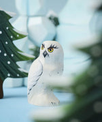 A close up of the Bumbu Toys Snowy Owl in a small world play scene. Other Bumbu toys can be seen blurred in the background.