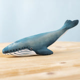 A Bumbu Toys Blue Whale handmade wooden toy figure placed on a wooden surface. We stock a wide range of handmade wooden toy figures here at Babipur. 