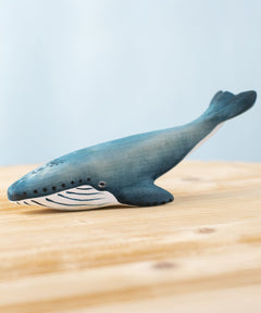 A Bumbu Toys Blue Whale handmade wooden toy figure placed on a wooden surface. We stock a wide range of handmade wooden toy figures here at Babipur. 
