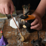 A child holding the Bumbu witch and broom in their hand. The child is pretending to sweep a wooden surface underneath. These expertly hand crafted items are part of a large range of wooden toys available here at Babipur. 