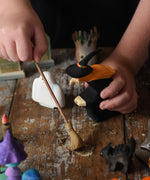 A child holding the Bumbu witch and broom in their hand. The child is pretending to sweep a wooden surface underneath. These expertly hand crafted items are part of a large range of wooden toys available here at Babipur. 
