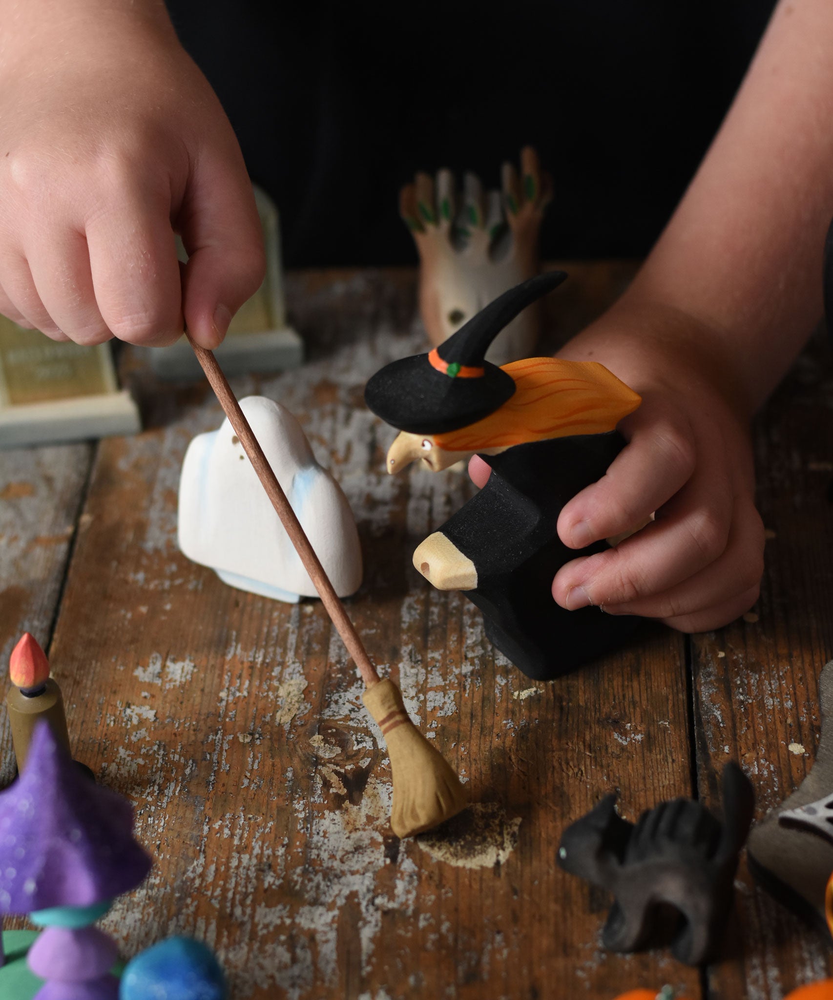 A child holding the Bumbu witch and broom in their hand. The child is pretending to sweep a wooden surface underneath. These expertly hand crafted items are part of a large range of wooden toys available here at Babipur. 