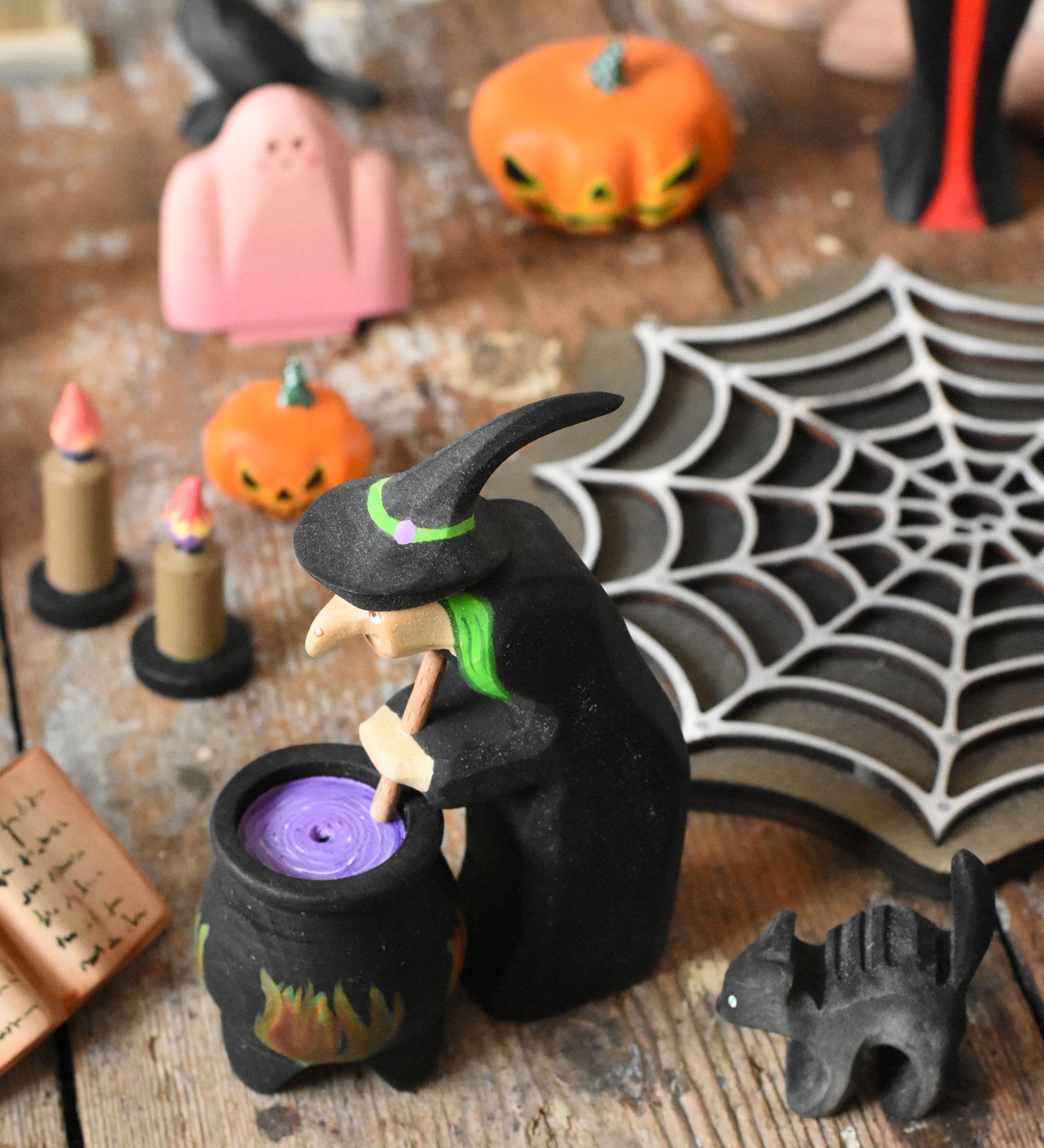 A Bumbu wooden witch standing next to a wooden cauldron in a halloween  small world play scene. These expertly hand crafted items are part of a large range of wooden toys available here at Babipur. 