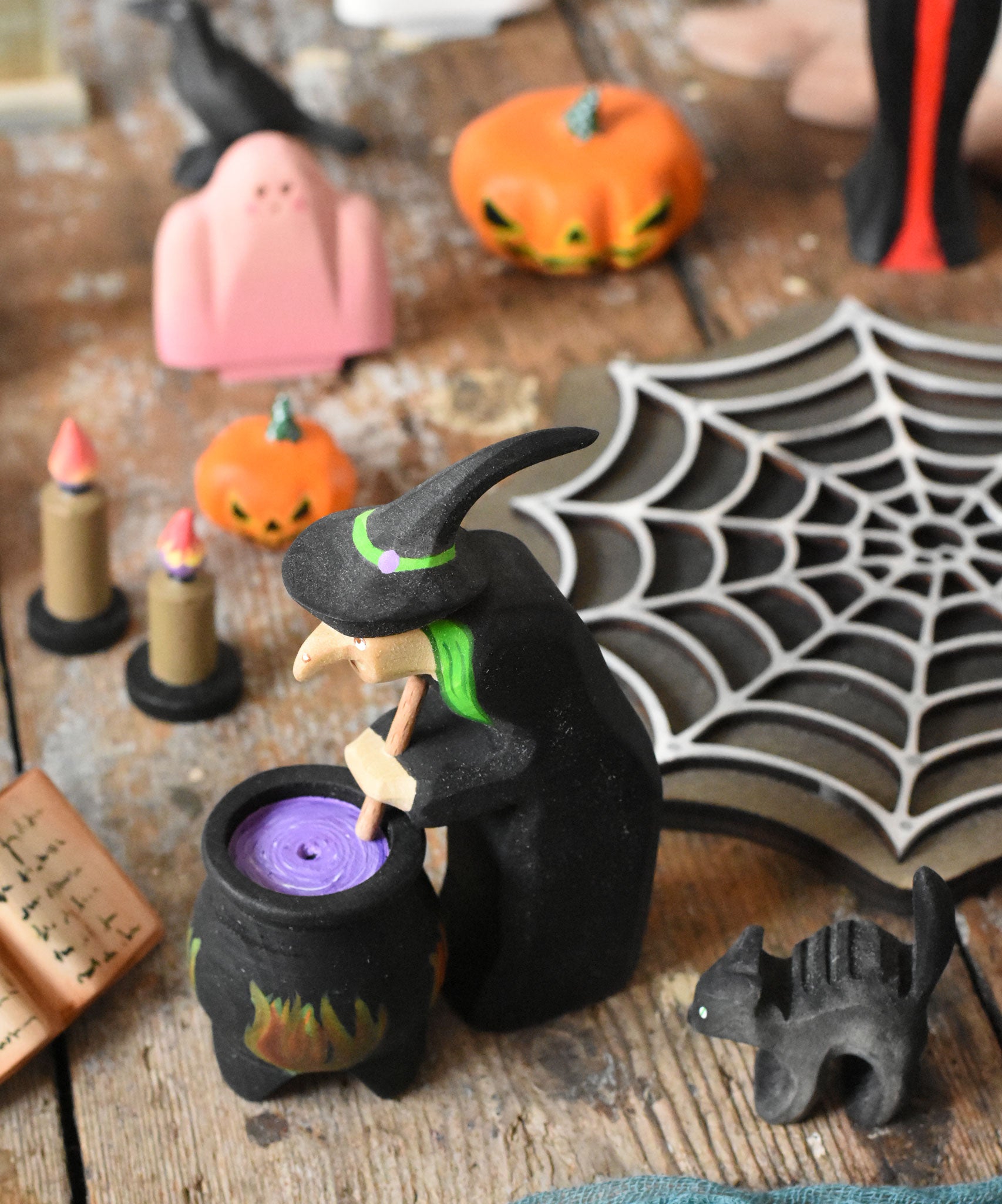 A Bumbu wooden witch standing next to a wooden cauldron in a halloween  small world play scene. These expertly hand crafted items are part of a large range of wooden toys available here at Babipur. 