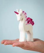 A Bumbu Toys Pastel Baby Unicorn wooden figure in the palm of an adult's hand