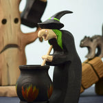A Bumbu Toys brewing witch figure standing in front of a Bumbu Cauldron in a spooky Halloween themed play scene. 