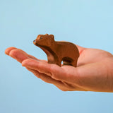 Adult hand holding the Bumbu toys handcrafted wooden brown standing cub bear showing scale