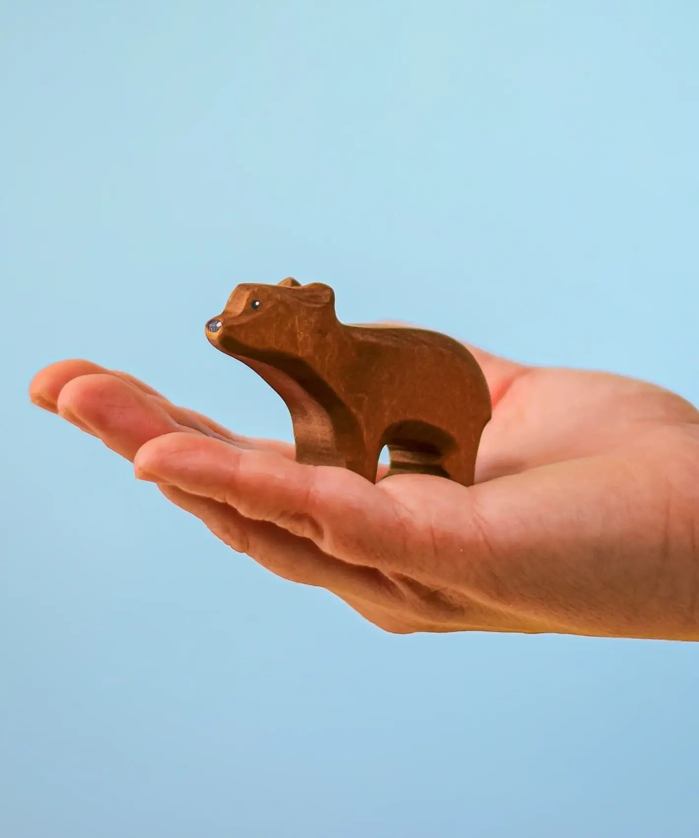 Adult hand holding the Bumbu toys handcrafted wooden brown standing cub bear showing scale