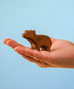 Adult hand holding the Bumbu toys handcrafted wooden brown standing cub bear showing scale