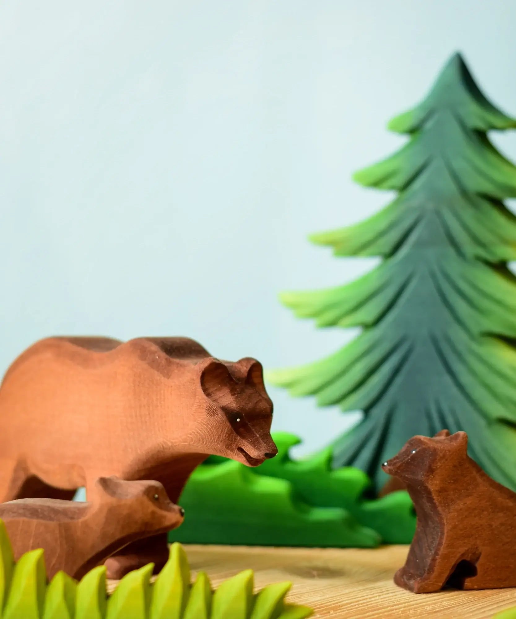 Play scene showing Bumbu toys handcrafted wooden brown standing bears and a fir tree figure in the background