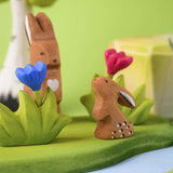 The Bumbu Toys wooden baby rabbit, in a curious upright position and surrounded by Bumbu wooden creatures and nature