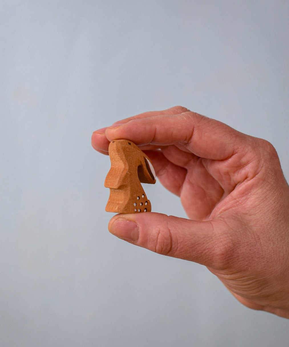 The Bumbu Toys wooden baby rabbit, in a curious upright position, held in a hand for size reference