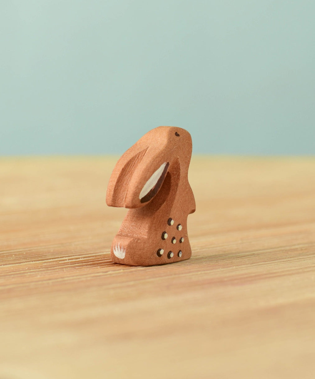 A back view of The Bumbu Toys wooden baby rabbit, in a curious upright position.