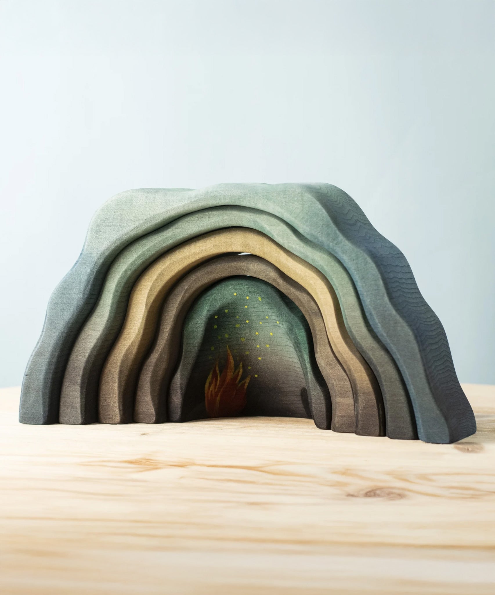 Bumbu Toys Dragon's Cave wooden toy figure placed on a wooden surface. The wooden cave is part of a large range of Handmade wooden figures from Bumbu that are available here at Babipur. 