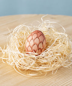 A Bumbu wooden egg placed in a wooden wool nest on a wooden surface. 