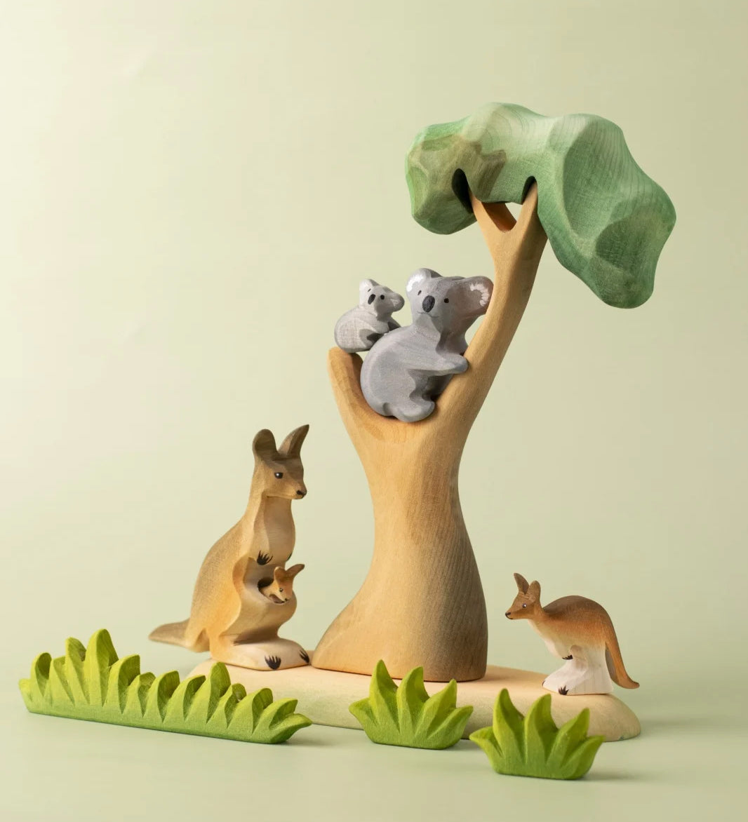 A small world play scene with the Bumbu Toys Eucalyptus Tree at the centre. The scene features a koala and it's cub along with kangaroos and wooden grass style greenery. 