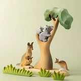 A small world play scene with the Bumbu Toys Eucalyptus Tree at the centre. The scene features a koala and it's cub along with kangaroos and wooden grass style greenery. 