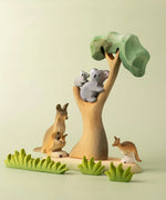 A small world play scene with the Bumbu Toys Eucalyptus Tree at the centre. The scene features a koala and it's cub along with kangaroos and wooden grass style greenery. 