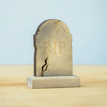 The RIP decorated headstone from the Bumbu Toys Gravestones Set. The headstone is placed on a wooden surface.