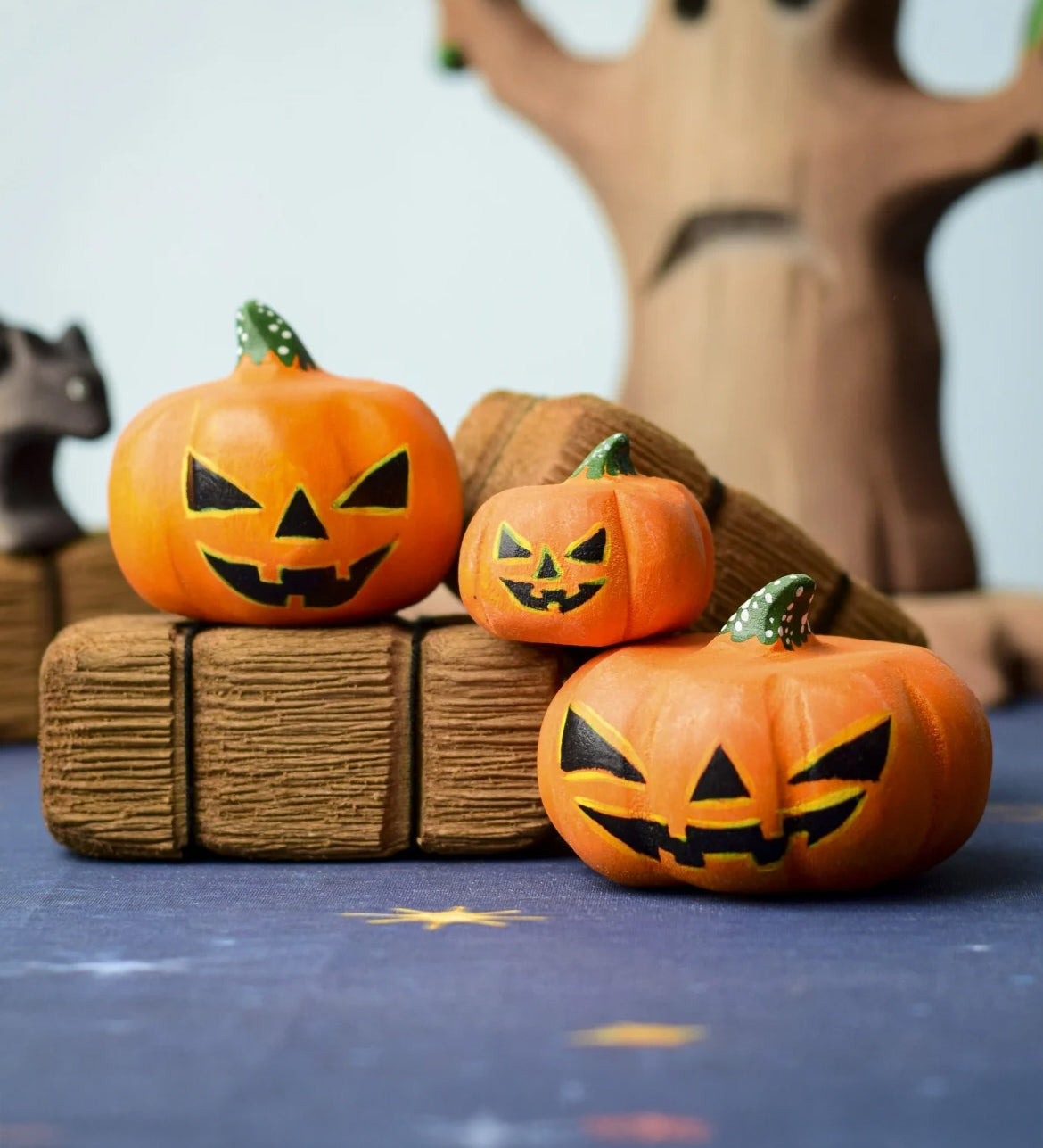 The Bumbu Toys Halloween Pumpkins Set placed in a small world play scvene with other wooden Bumbu toys including hay bales and a spooky tree in the background. 