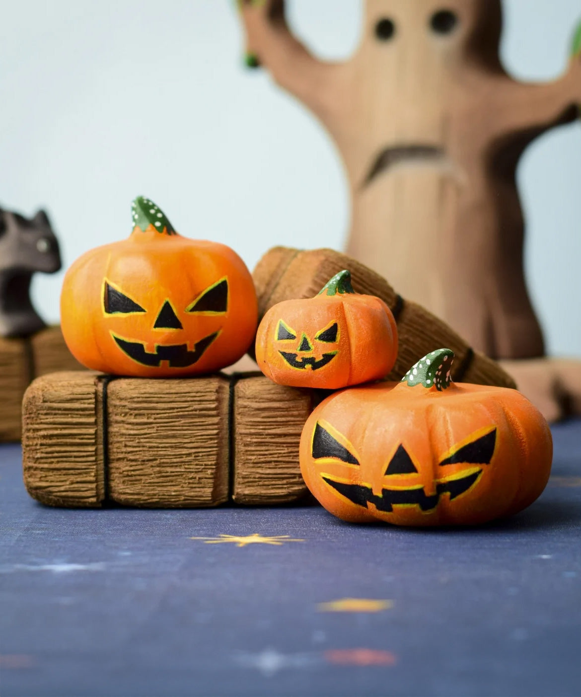 The Bumbu Toys Halloween Pumpkins Set placed in a small world play scvene with other wooden Bumbu toys including hay bales and a spooky tree in the background. 