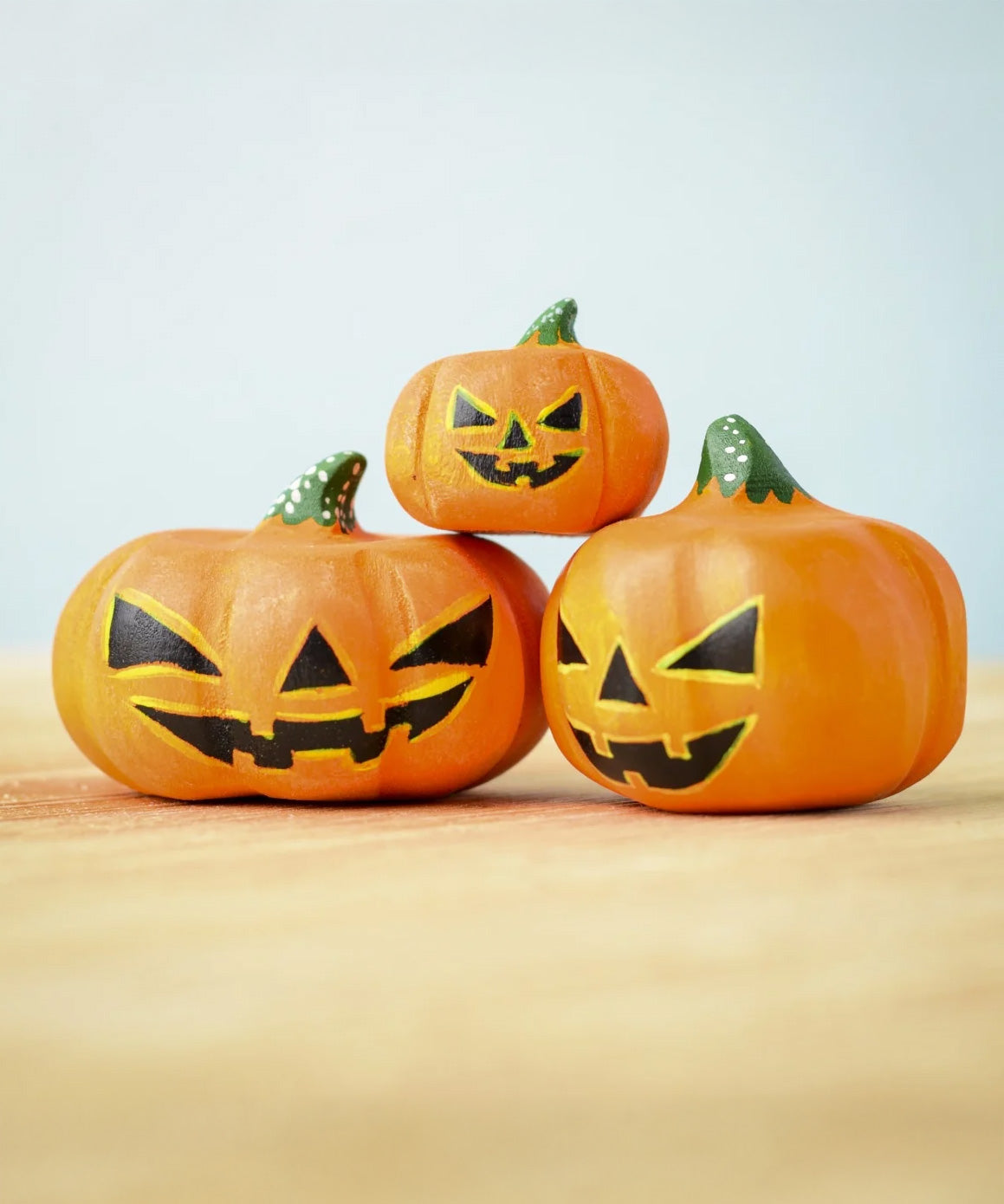 The Set of 3 Bumbu Toys Halloween Pumpkins placed on a wooden surface. The pumpkins all have black painted carving effect details.